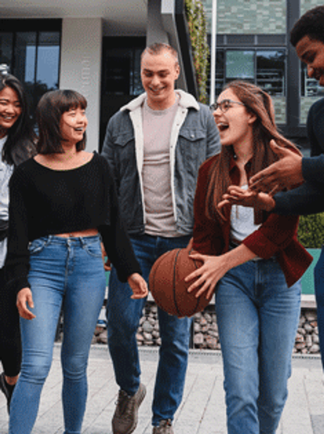 A diverse group of young adults walking together in a park, chatting and laughing, enjoying each other's company.