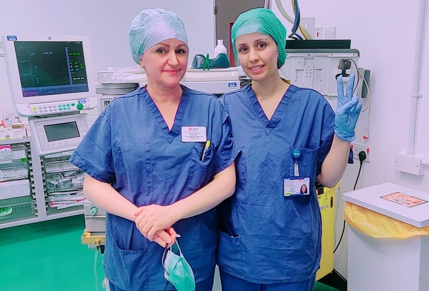 Two women in medical scrub suits standing next to each other in a hospital hallway.