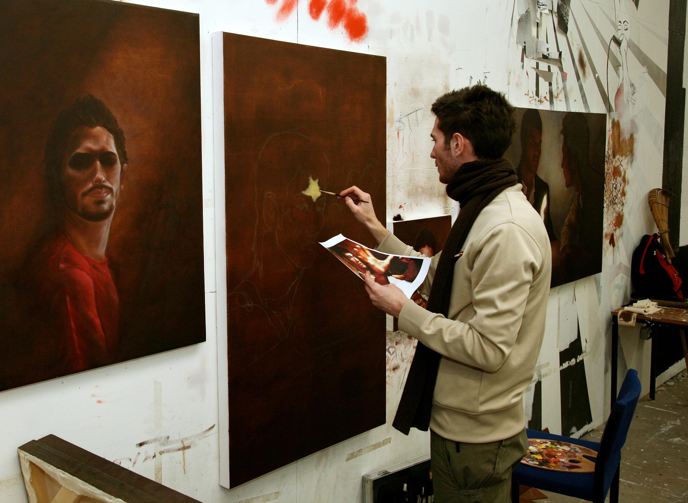 student painting in studio, copying image of Bruce Lee they hold in their hands