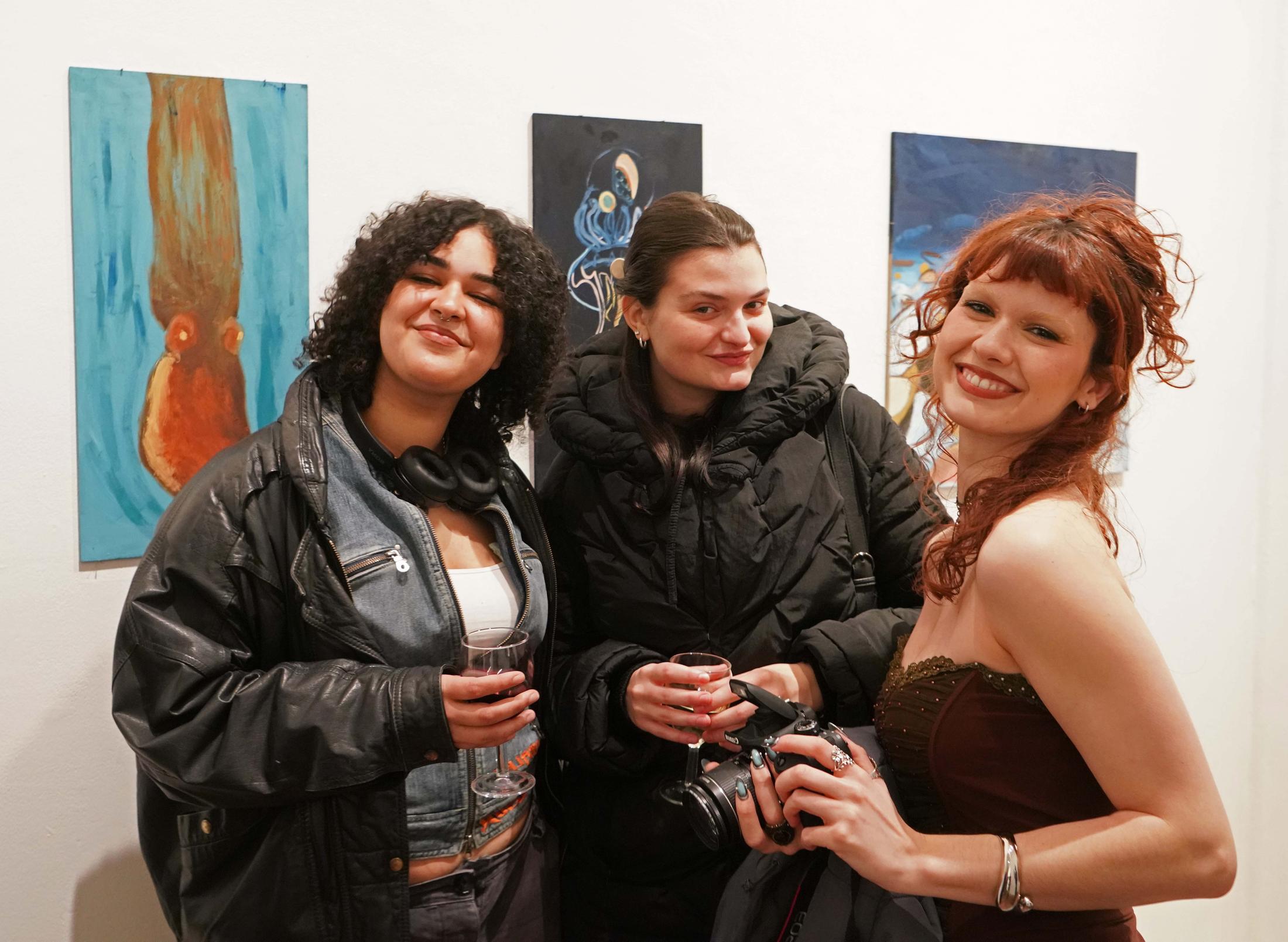 Three students smiling at the camera at an art show
