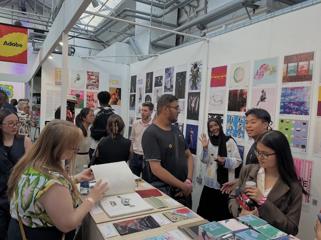 A photo of a stand at a design and advertising exhibition full of people of different ethnic backgrounds exhibiting and looking at the work